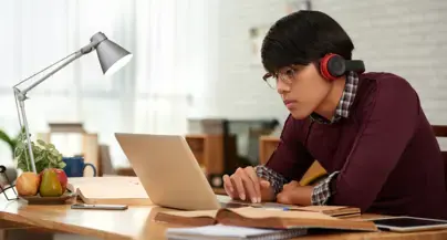 A student looks intently at their laptop with headphones on.