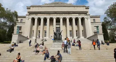 People walking and sitting on the steps of Low Library in the summer.