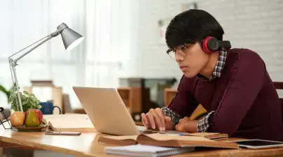 A student looks intently at their laptop with headphones on.